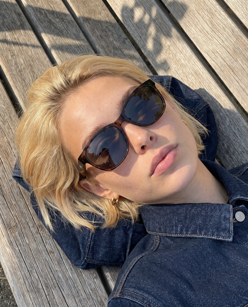 Woman lying on a wooden bench wearing Vibes Delta 9 tortoise sunglasses