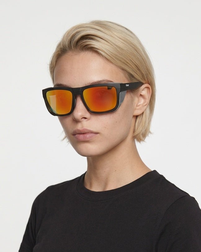 Juno side-shield wrap sunglasses in Orange / Black, orange lens on black frame, worn by a woman, front view