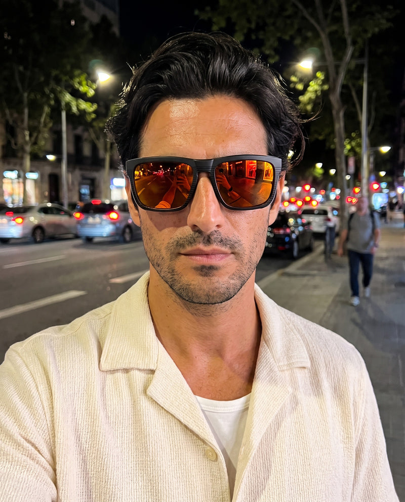 Man on a city street at night wearing Vibes Juno orange mirror sunglasses