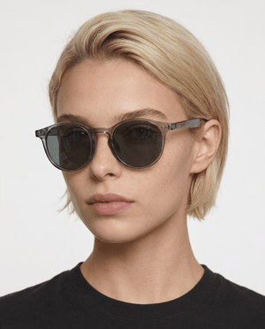 Onyx round retro sunglasses in Black / Clear Grey, black lens on clear grey frame, worn by a woman, front view